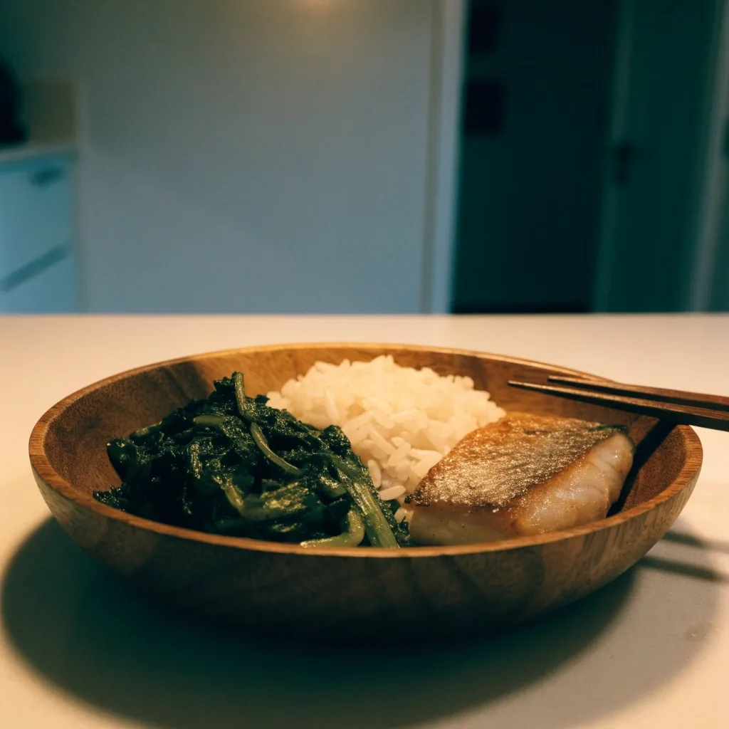 A wooden bowl with greens, rice and grilled fish arranged in separate portions